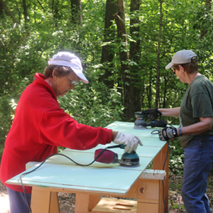 Two people using electric sanders on project.